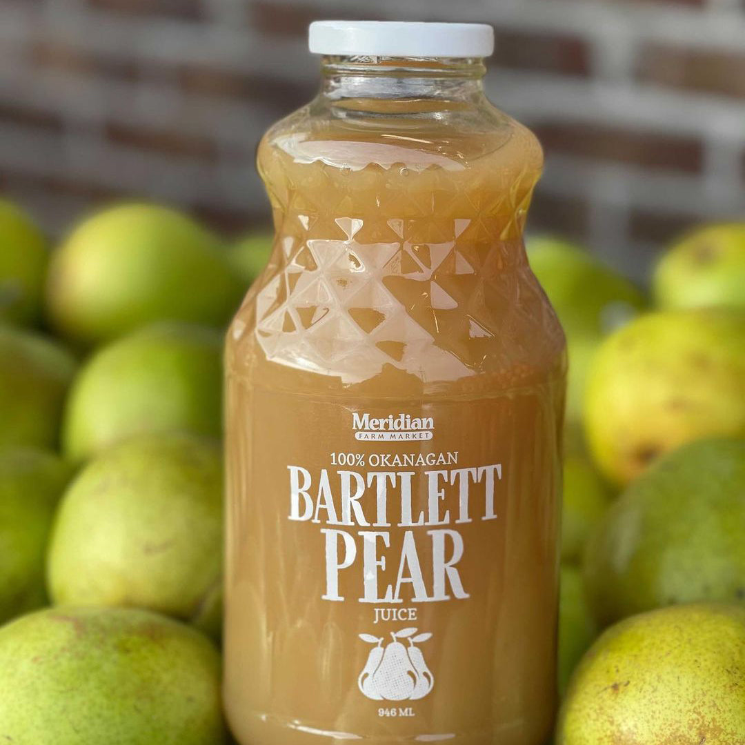 Meridian Farm Market Bartlett Juice 946 ml in front of Bartlett pears and a brick wall.