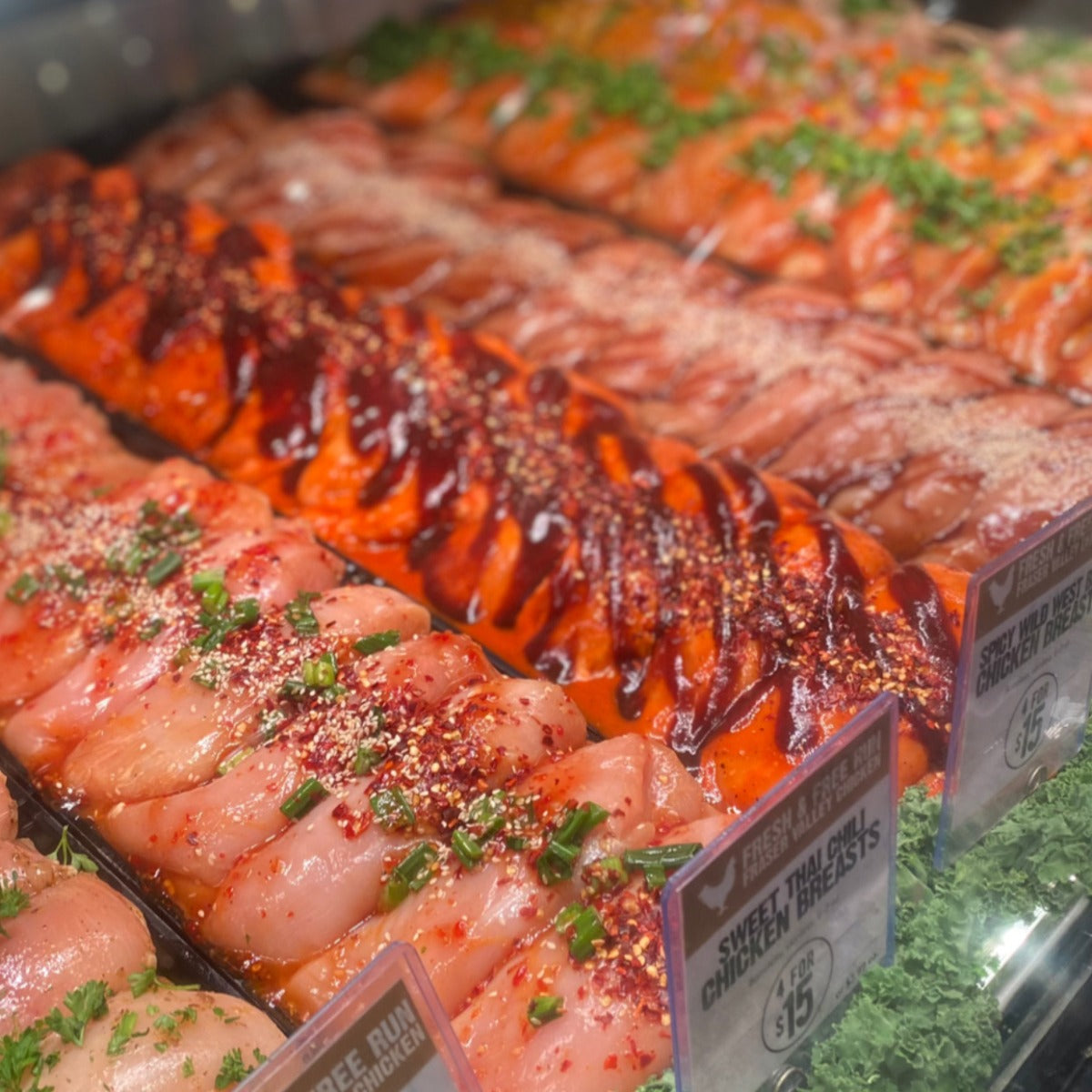 Raw chicken breasts marinated in buffalo sauce and garnished with bbq sauce and cayenne pepper.