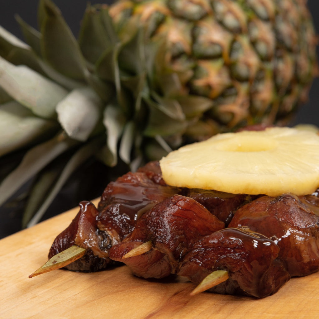 Maui pork skewers garnished with a pineapple ring with a pineapple in the background
