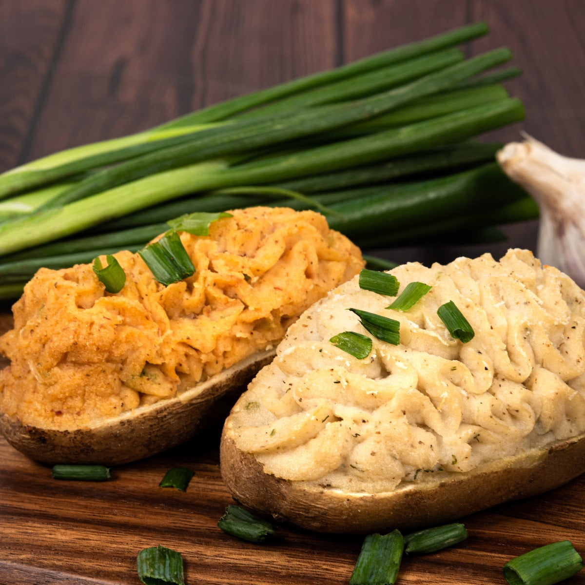 Baked bacon cheddar potato garnished in green onions next to baked parmesan garlic potato.