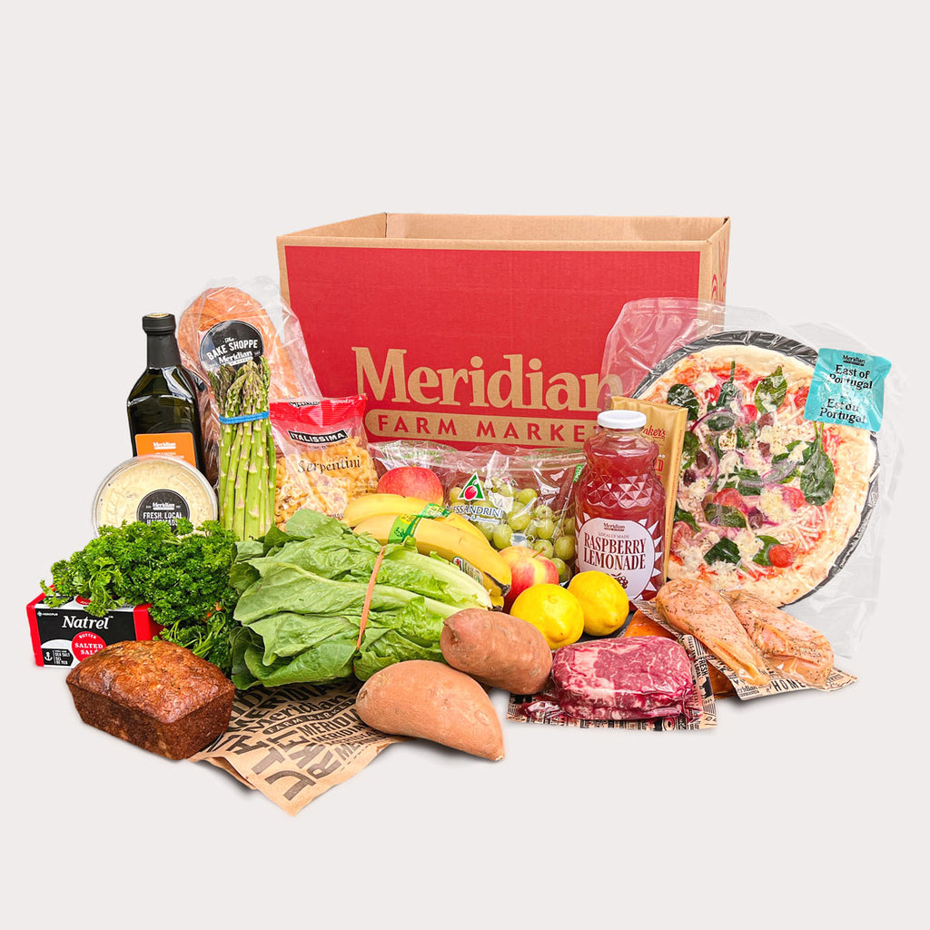 A wide selection of fresh groceries assembled in front of a red Meridian delivery box. Groceries include packaged steak and chicken breasts, fresh fruits and veggies, take-n-bake pizza, french bread, olive oil and more.