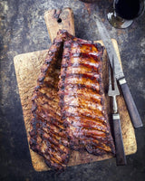 Cooked pork baby back ribs on a wooden cutting board ready to be sliced and served