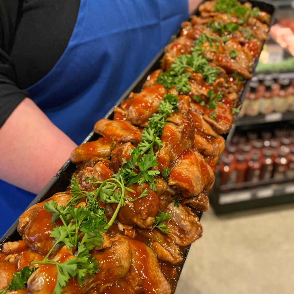 Chicken wings marinated in honey garlic sauce garnished with parsley in a large black tray.