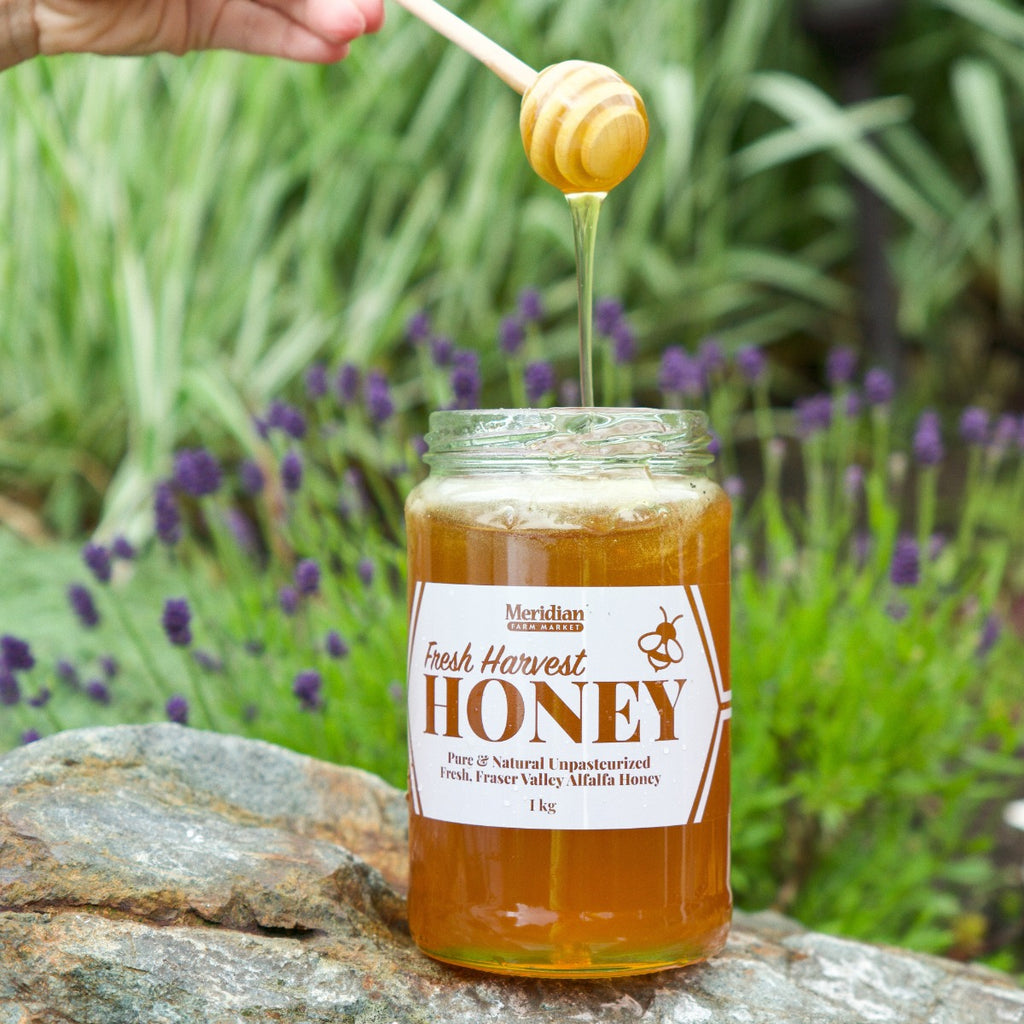 A honey dipper drizzling honey into a bottle of Meridian Farm Market Fresh Harvest Honey. 