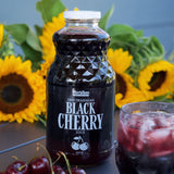 Black Cherry Juice 946ml placed on a table with cherries and juice poured into a cup.