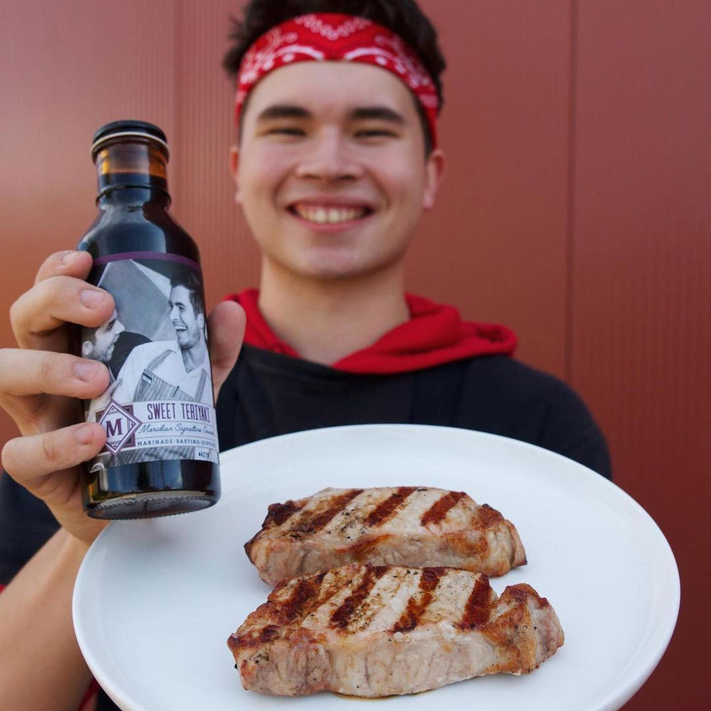 Meridian Farm Market worker holding up cooked plain porkchops and Meridian teriyaki sauce on a plate.