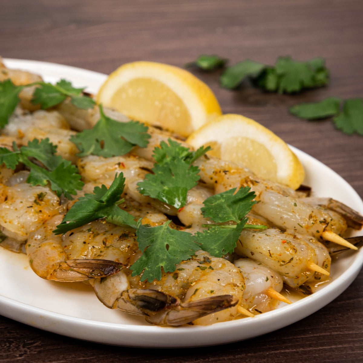 Lemon herb prawn skewers garnished with parsley and lemons on a plate. 
